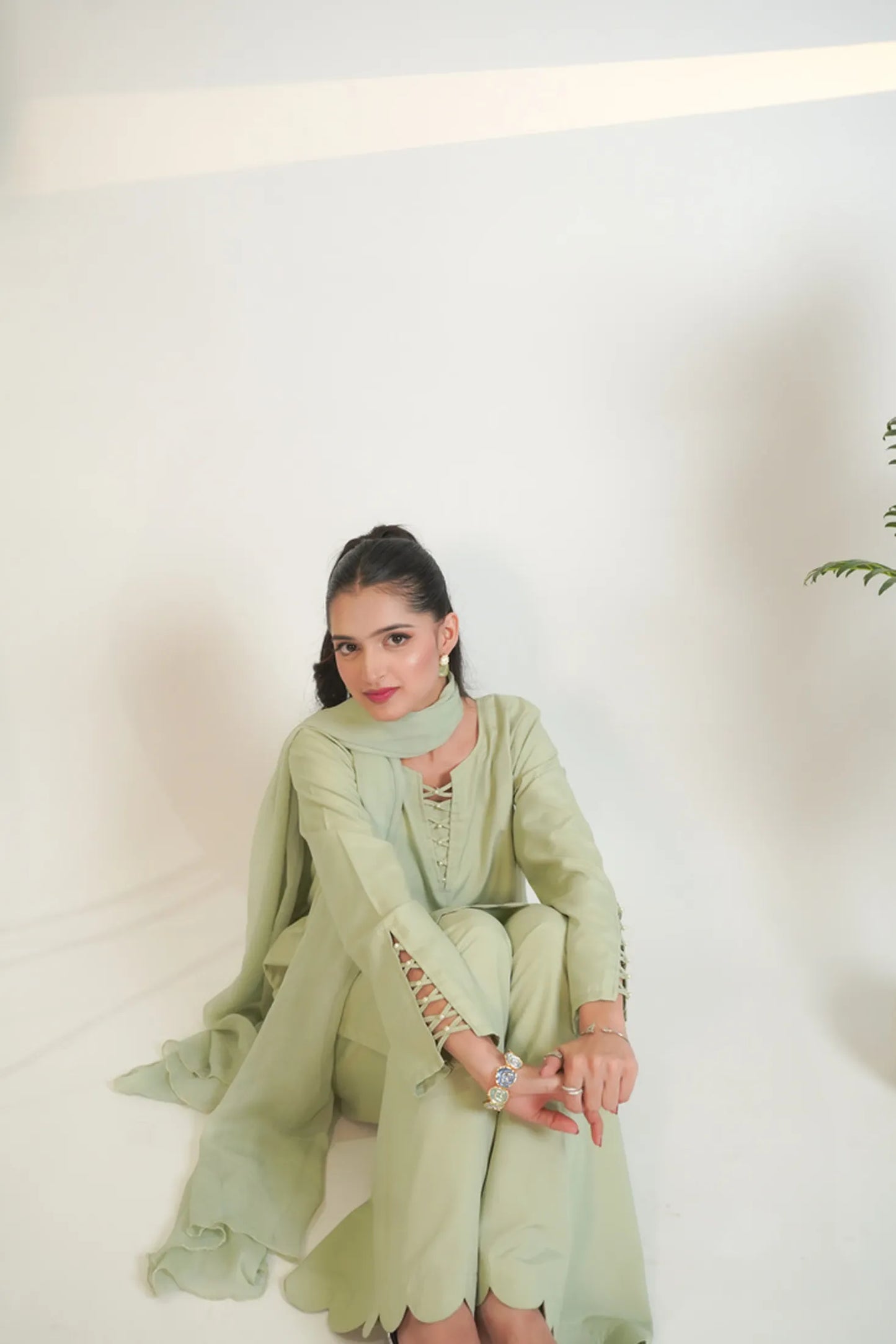 Woman in a light green traditional outfit sitting against a white background