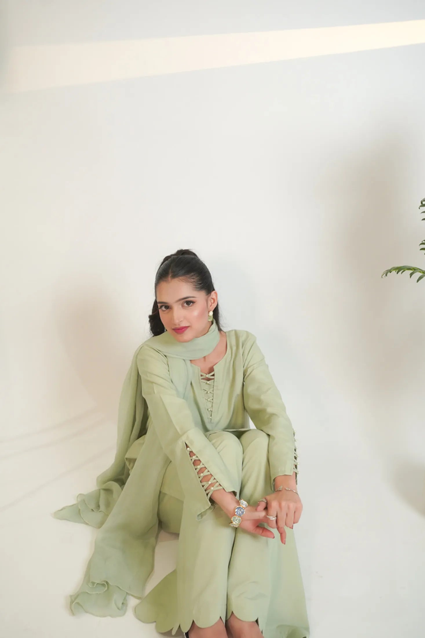 Woman in a light green traditional outfit sitting against a white background
