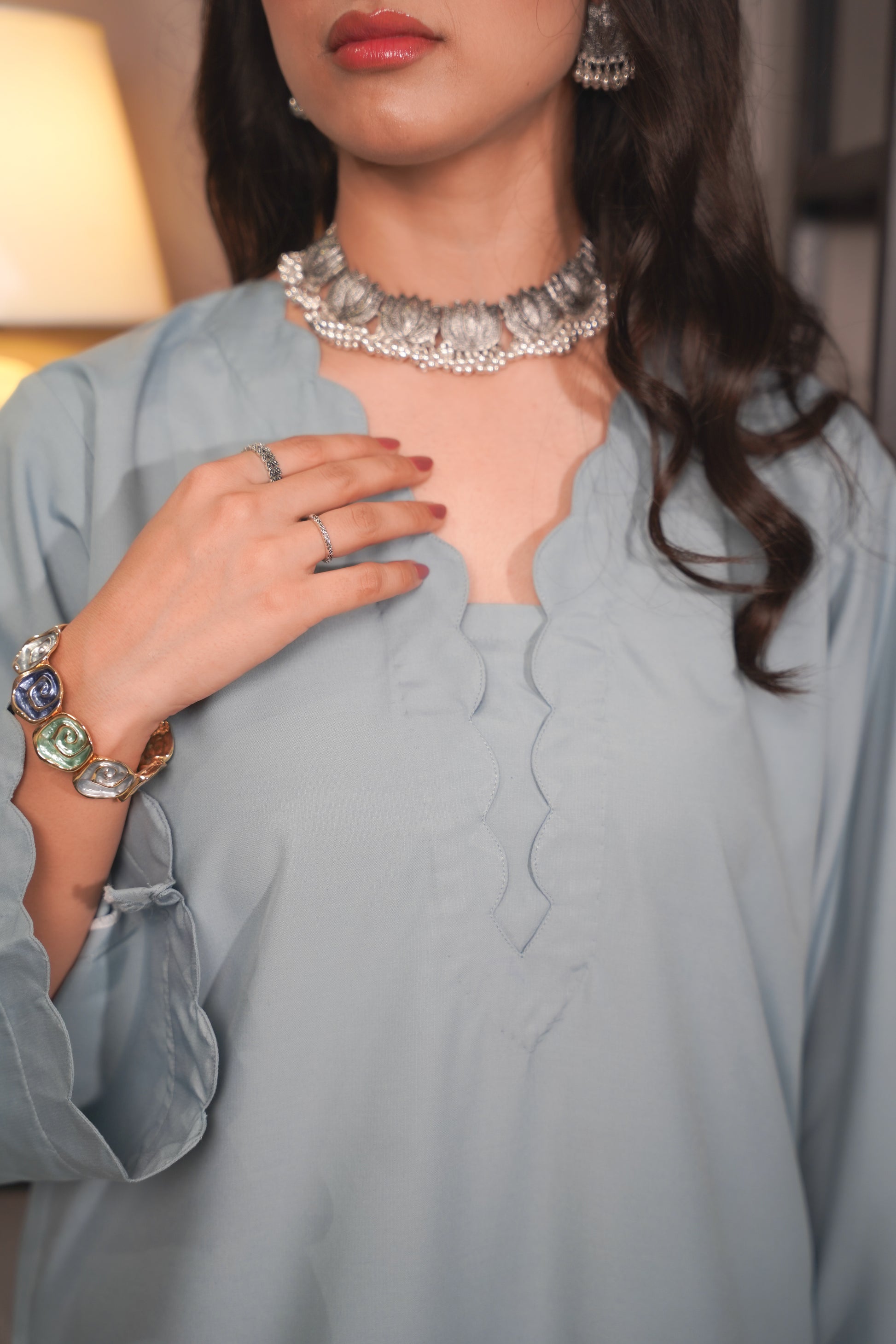 Woman wearing a light blue outfit with jewelry including a necklace, rings, and bracelets.