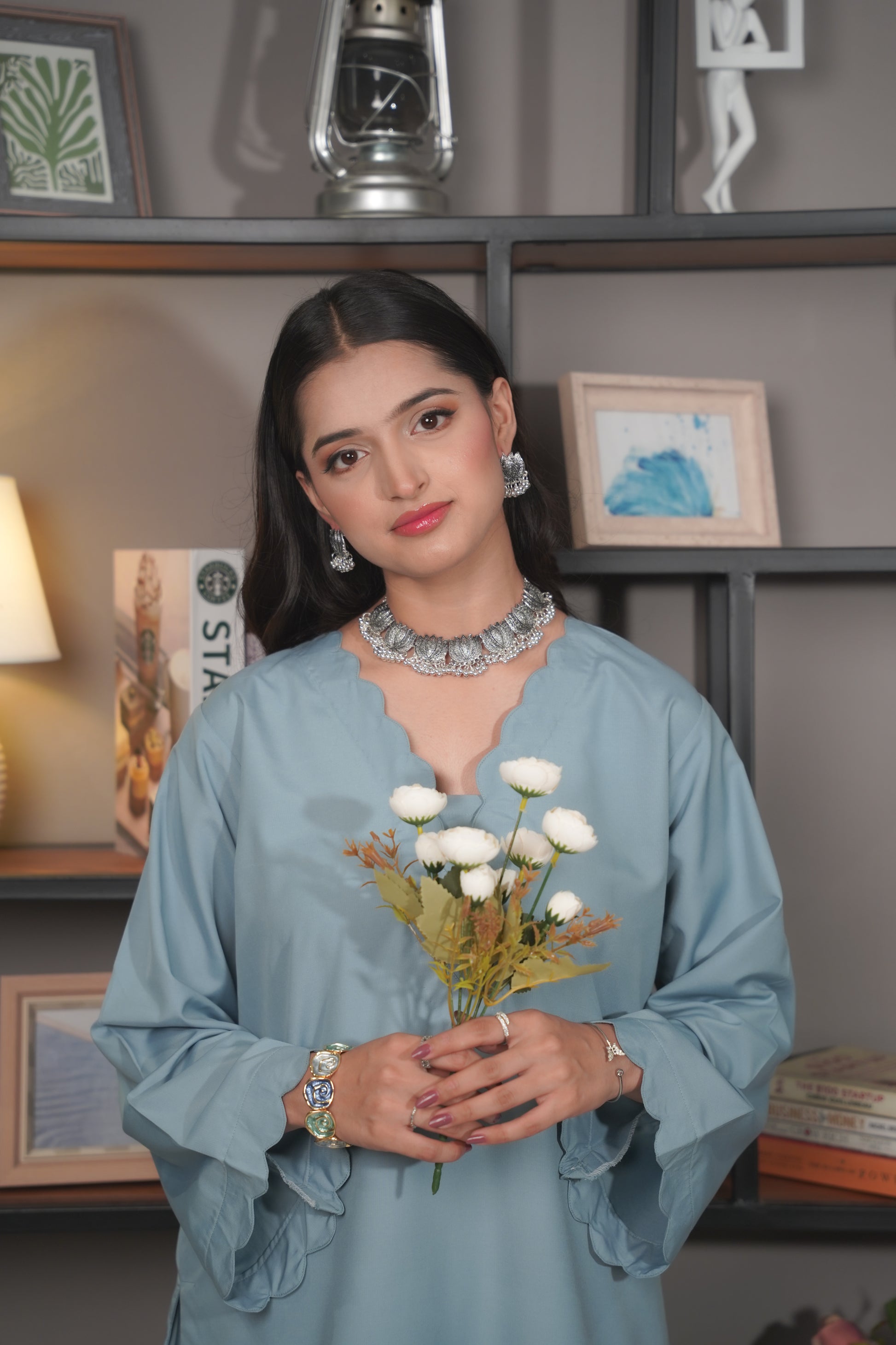 Woman holding flowers in a room with shelves and decor