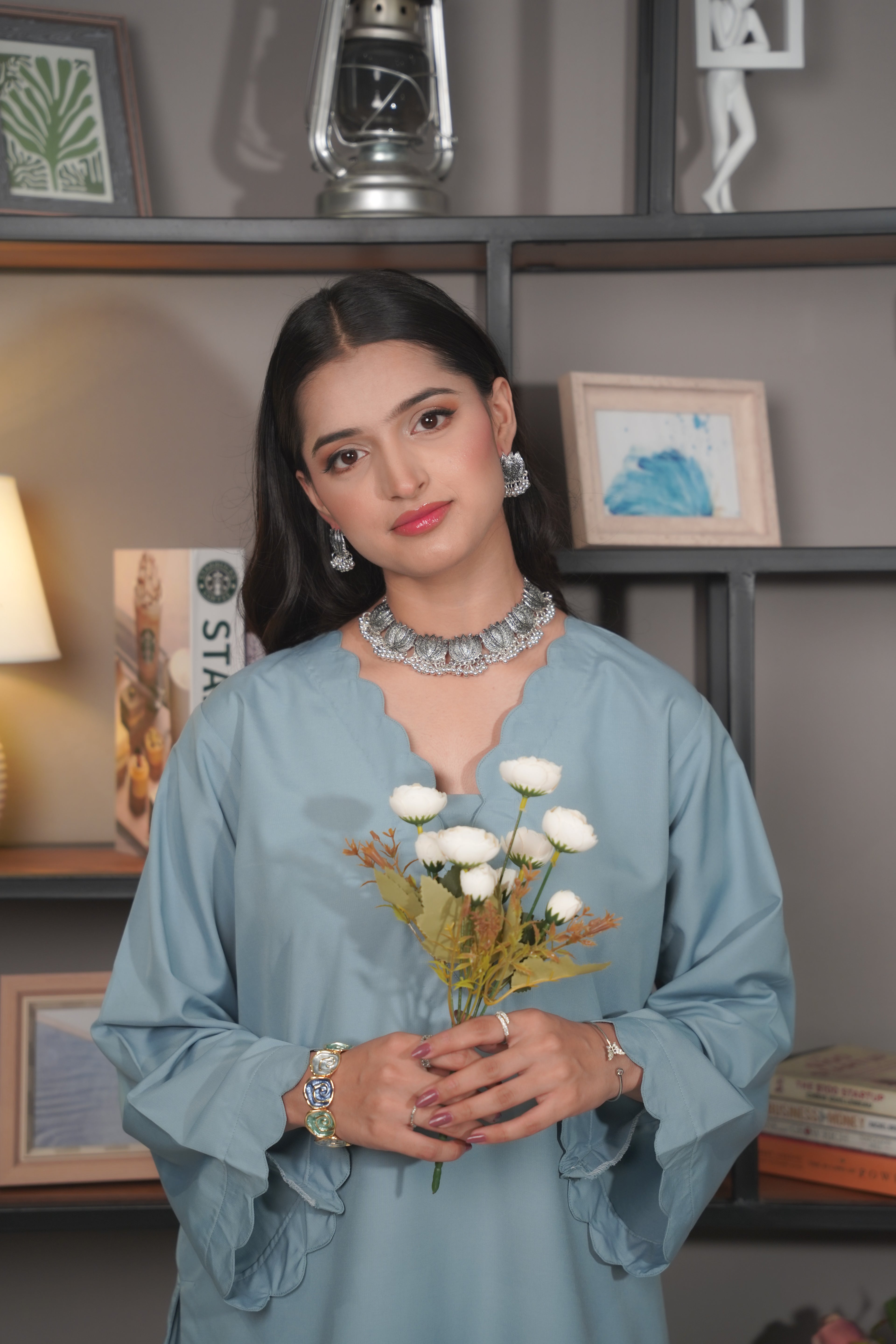 Woman holding flowers in a room with shelves and decor