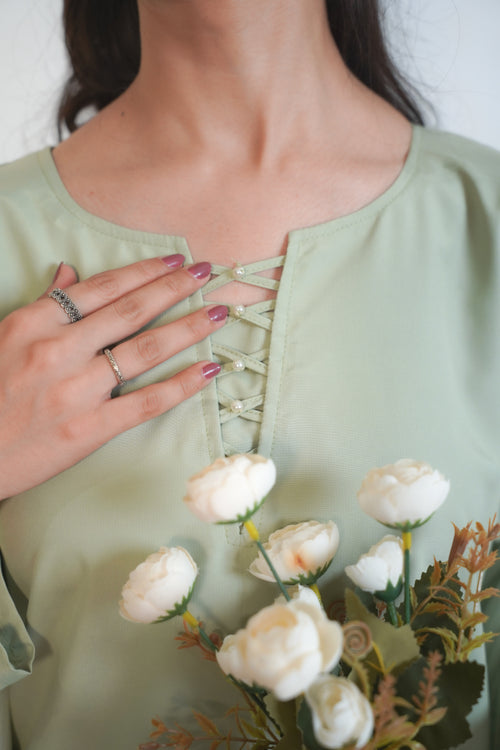Person wearing a light green blouse with lace-up detail, holding a bouquet of white flowers.