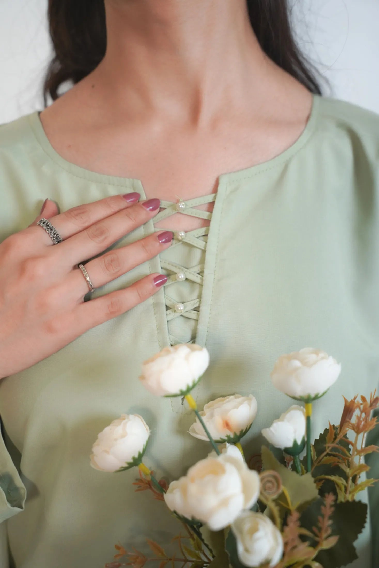 Person wearing a light green blouse with lace-up detail, holding a bouquet of white flowers.