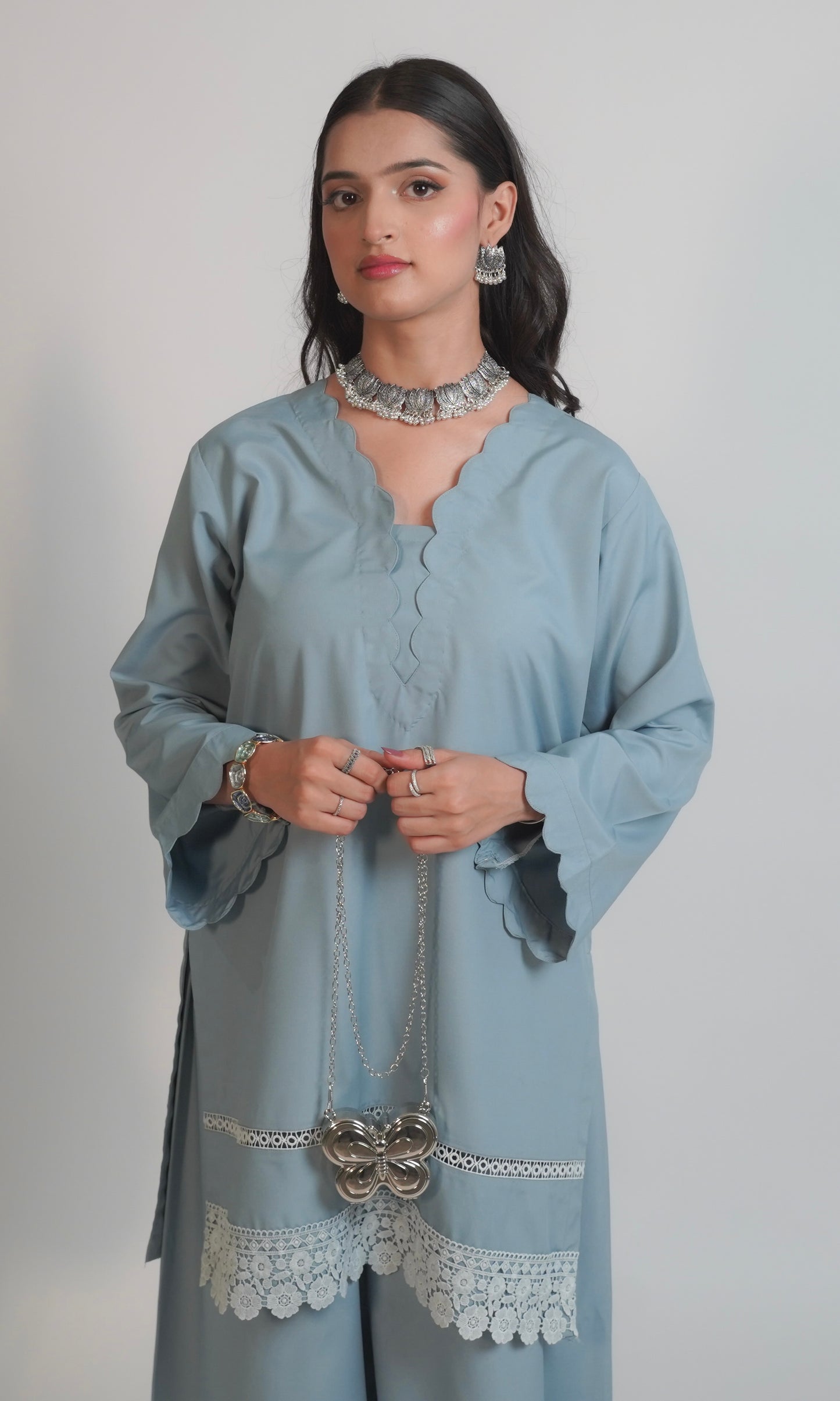 Woman wearing a light blue kurta with lace details on a plain background
