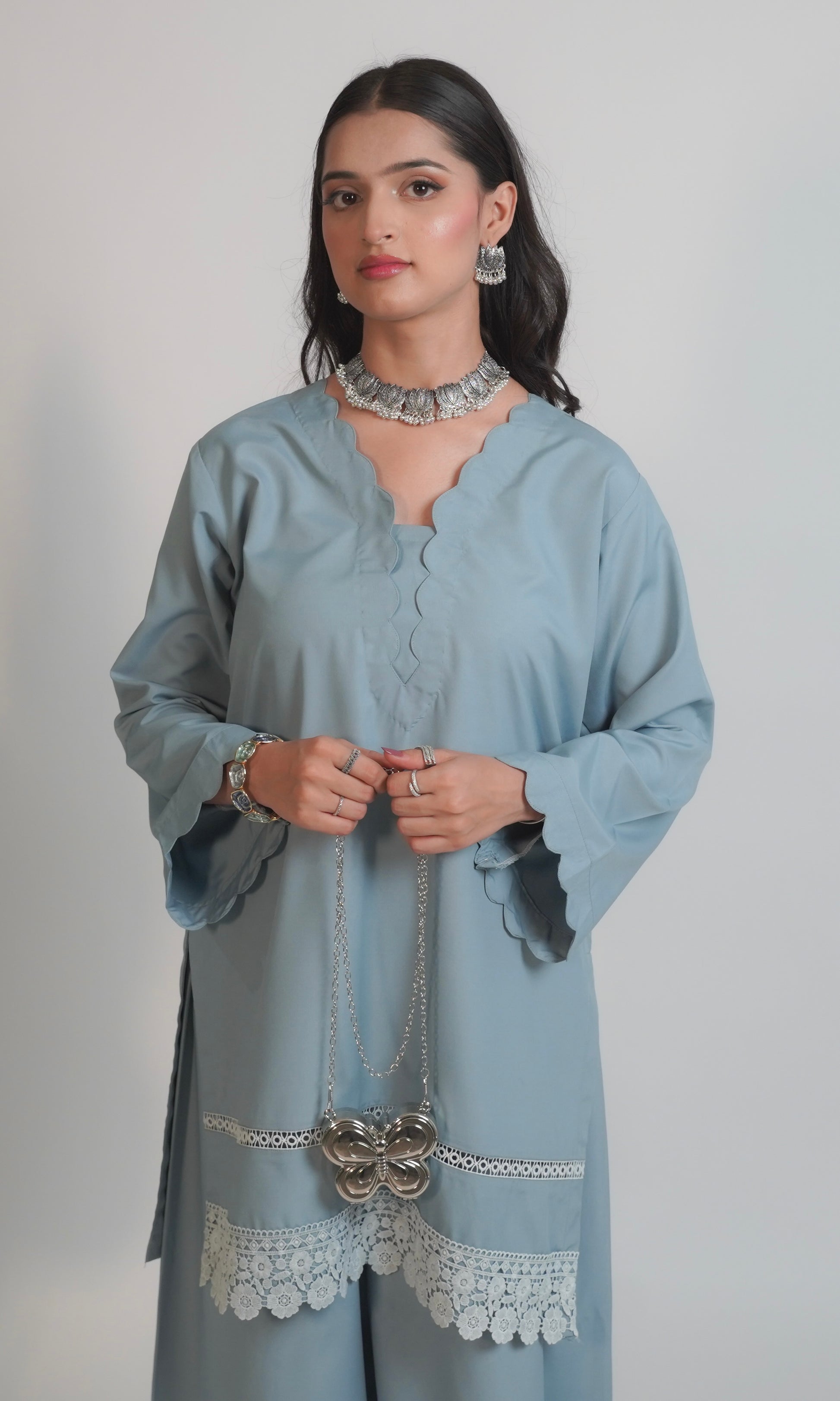 Woman wearing a light blue kurta with lace details on a plain background
