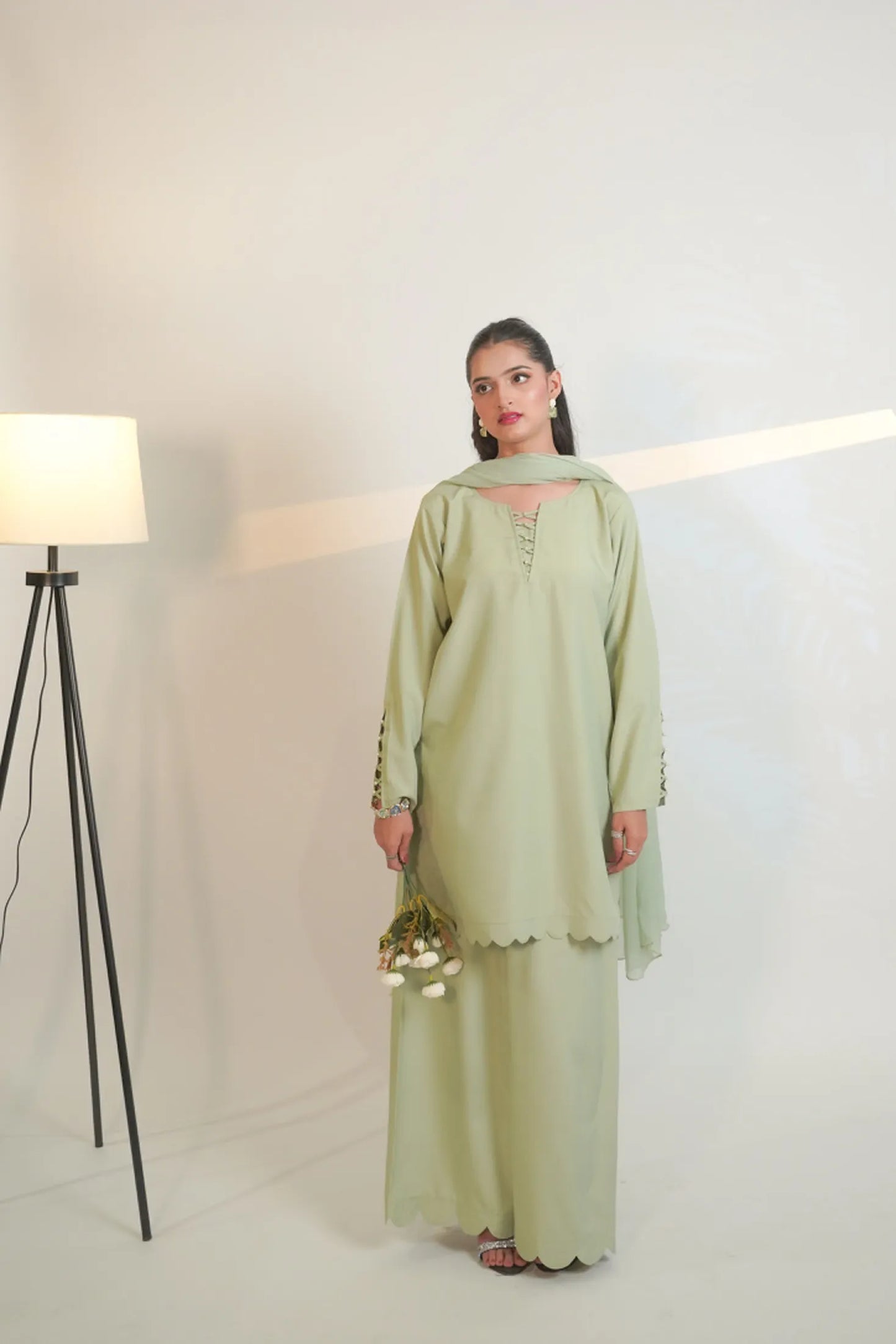 Woman wearing a light green traditional outfit with a plain background